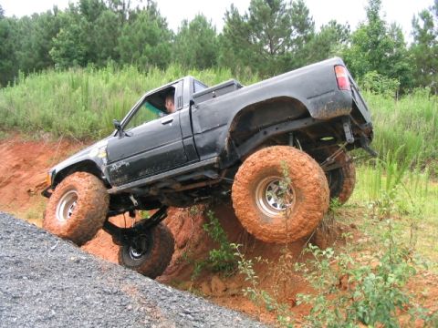 1986 Ford F-150 - A black pickup truck navigates a steep dirt path with its wheels at extreme angles.