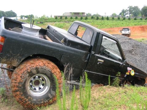 1986 Ford F-150 - A black pickup truck is stuck in the mud, with a white SUV visible in the distance on a dirt mound.