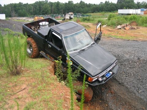 1986 Ford F-150 - Pickup truck with oversized tires is stuck in a ditch off-road.