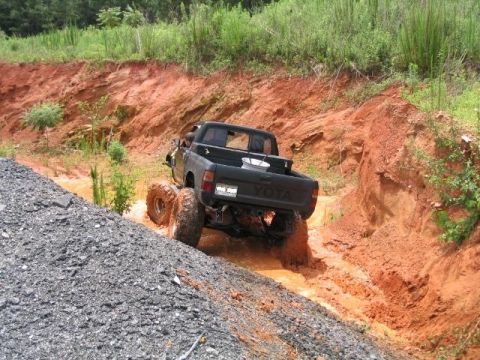 1986 Ford F-150 - A Toyota truck navigates a challenging muddy off-road course with steep, eroded banks.