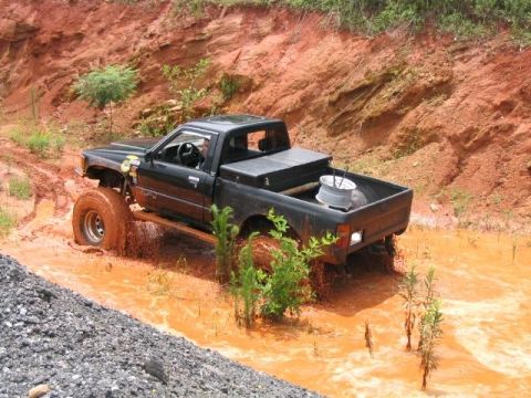 1986 Ford F-150 - A modified black pickup truck navigates a muddy off-road course with large tires.