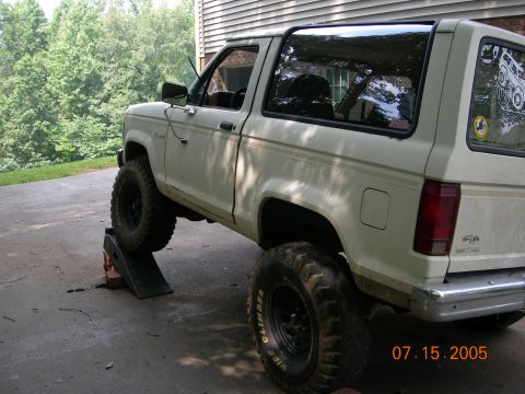 1984 Ford Bronco II - A white 1984 Ford Bronco II is shown with its front wheels elevated on ramps, highlighting its lifted suspension.