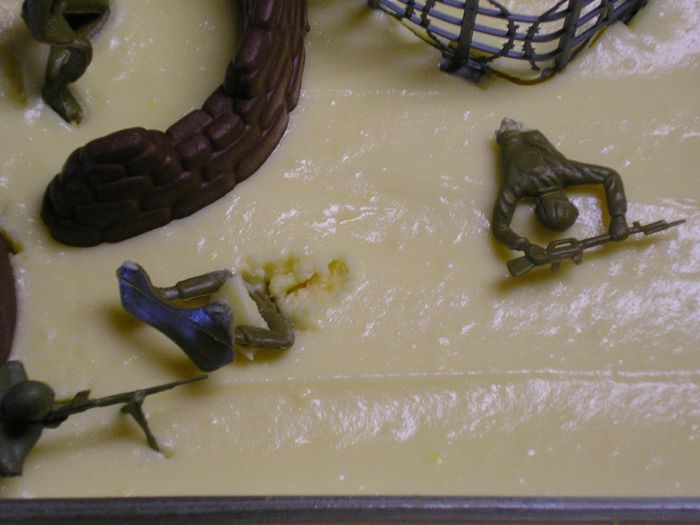 Toy soldiers scattered on a yellow surface with some debris and a brown tree-like object
