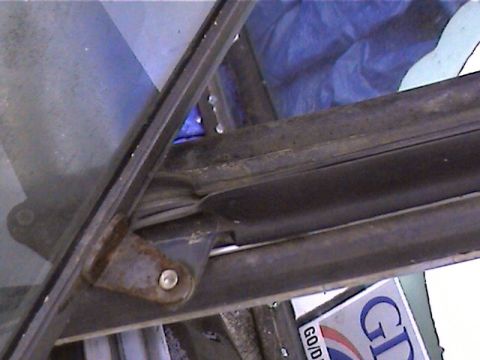 1978 Ford Bronco - Close-up of a vehicle's window frame hinge, showing signs of rust and a blue tarp in the background.