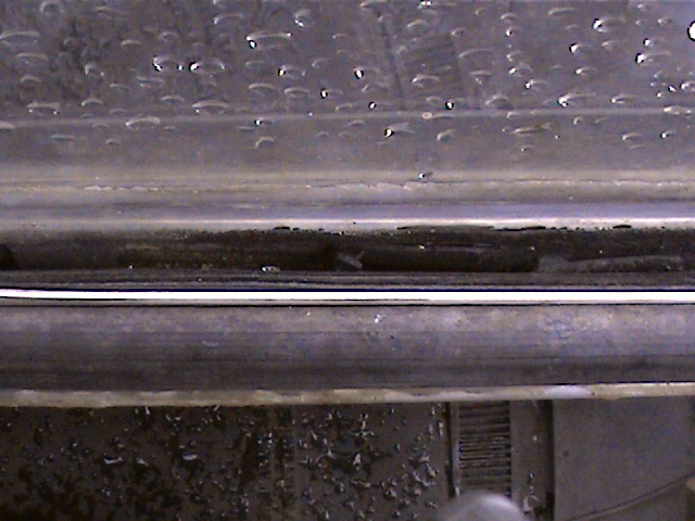 Close-up of a vehicle's door sill with water droplets on the window above