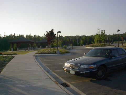 1985 Mercury Grand Marquis - Sedan parked in a lot near gazebos and trees under a clear sky.