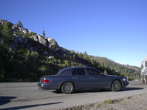 1985 Mercury Grand Marquis - A dark blue 1996 Mercury Grand Marquis sedan is parked on the side of a road, with a mountainous landscape under a clear blue sky.