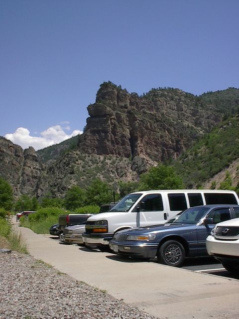 1985 Mercury Grand Marquis - Several vehicles are parked in a lot with a dramatic mountain range and blue sky in the background.