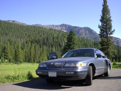 1985 Mercury Grand Marquis - A Mercury Grand Marquis is parked on the side of a road with a scenic mountain backdrop.