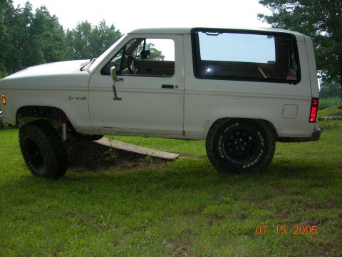 1984 Ford Bronco II - A white 1984 Ford Bronco II is shown in profile, a lifted suspension and off-road tires, parked on grassy terrain.