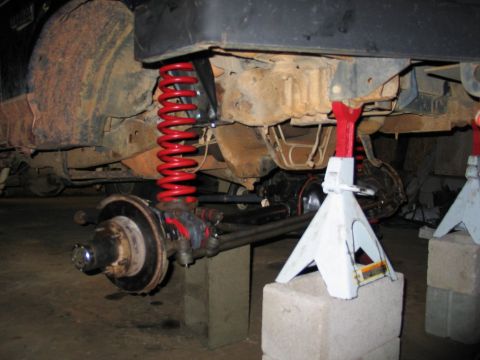 1995 Ford Bronco - The vehicle's undercarriage is visible, showing suspension components and rust. It is elevated on jack stands for maintenance.