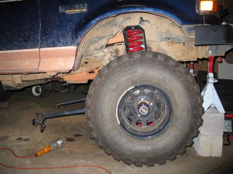 1995 Ford Bronco - The side of a blue 1995 Ford Bronco is shown with a large tire and red coilover suspension, indicating modifications.