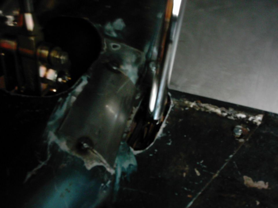 Close-up of vehicle interior with metal tubing and dark flooring, showing welding marks and some white sealant