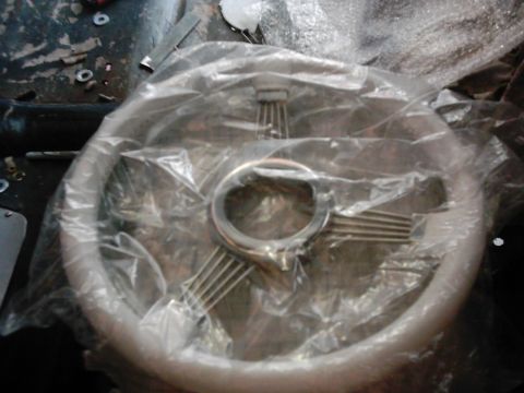 1978 Ford Bronco - A steering wheel, wrapped in plastic, with chrome spokes and a silver rim, is shown on a dark surface.