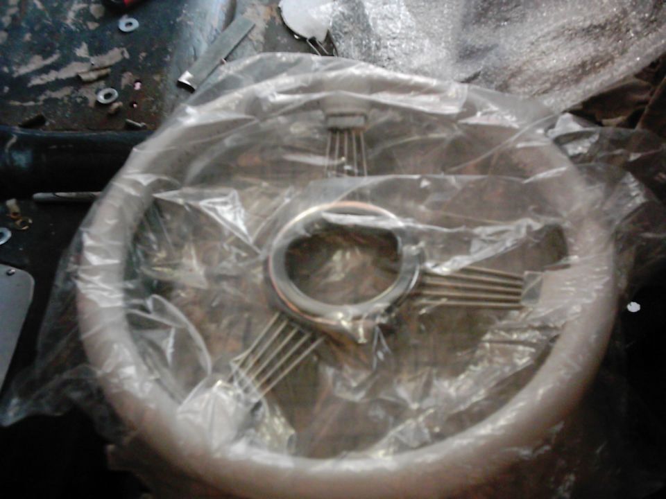 Steering wheel in plastic wrap, chrome spokes, silver rim, on a dark surface