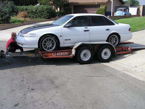 1993 Ford Taurus - White 1993 Ford Taurus being loaded onto a U-Haul trailer by a person.