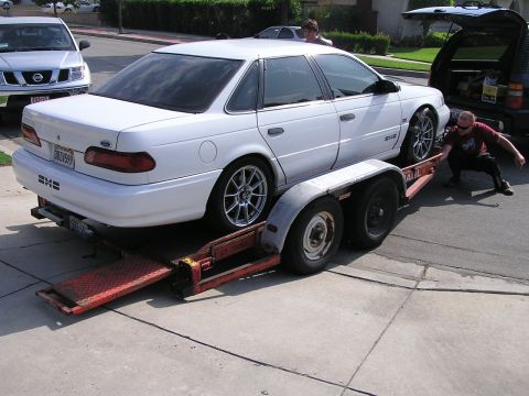 1993 Ford Taurus - A white 1993 Ford Taurus is being loaded onto a trailer, with a person assisting and an SUV in the background.