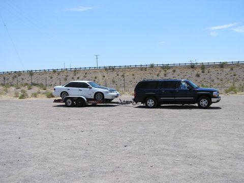 1993 Ford Taurus - A dark blue SUV tows a white sedan on a U-Haul trailer under a clear blue sky.