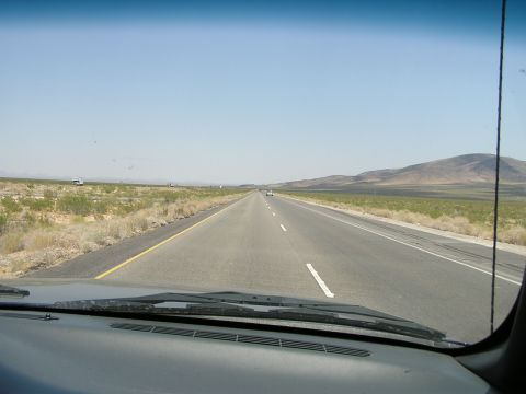 1993 Ford Taurus - Driving down a desolate highway with sparse vegetation and distant mountains under a bright, cloudless sky.