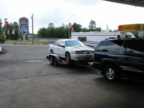 1993 Ford Taurus - A white 1993 Ford Taurus is transported on a trailer by a dark SUV.