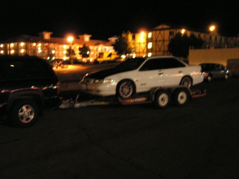1993 Ford Taurus - A white 1993 Ford Taurus sedan is transported on a trailer at night, with a black hood and aftermarket wheels.