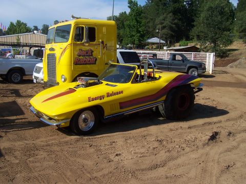 1994 Ford F-150 - A modified yellow 1965 Chevrolet Corvette convertible is parked in a dirt lot with a large yellow truck and other vehicles.