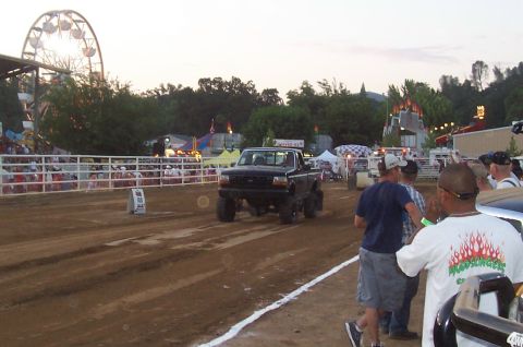 1994 Ford F-150 - A black 1994 Ford F-150 pickup truck competes on a dirt track at a fair with a Ferris wheel in the background.
