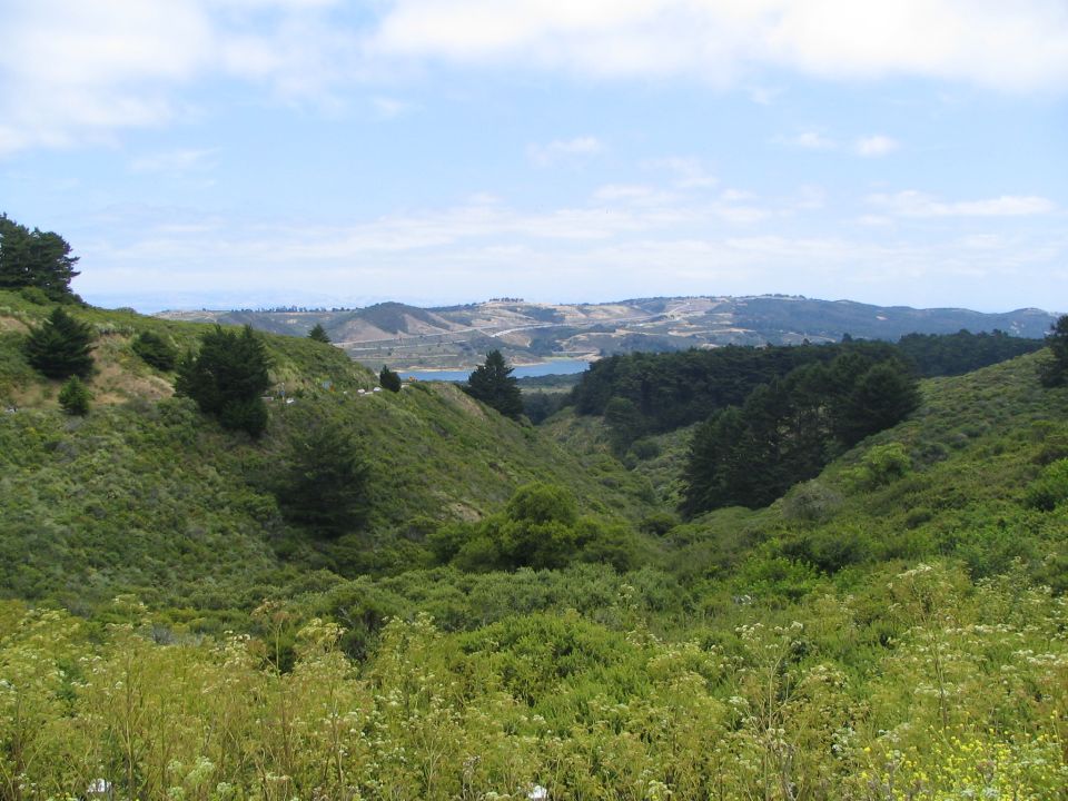 Scenic landscape with rolling green hills and a distant body of water under a partly cloudy sky