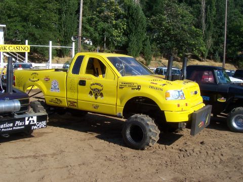1994 Ford F-150 - This modified yellow Ford F-150 features oversized tires, dual exhaust stacks, and custom decals.