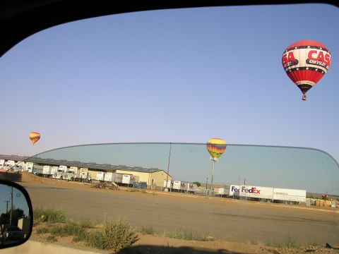 1993 Ford Taurus - Hot air balloons drift over a logistics yard filled with trucks under a clear blue sky.