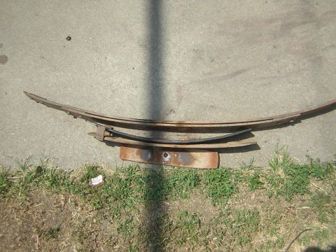 1995 Ford Bronco - A disassembled multi-leaf spring pack laid out on a concrete driveway at the edge of a lawn, with the individual rusty leaves separated and…