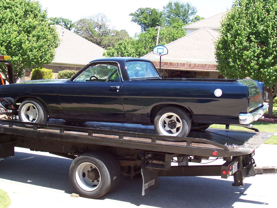 Dark Ford Ranchero car-pickup on a Century flatbed tow truck in a suburban street.