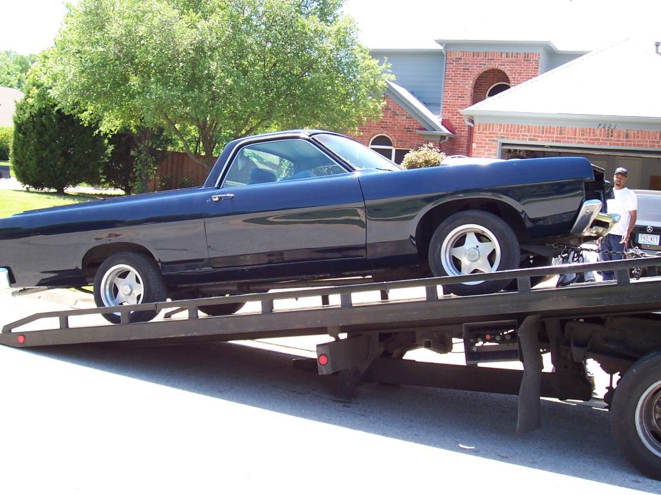Dark blue vintage Ford Ranchero pickup loaded on a flatbed tow truck, side view