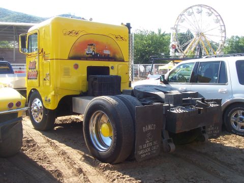 1994 Ford F-150 - A yellow semi-truck cab with a mural on its side is parked next to a white SUV, with a Ferris wheel in the background.