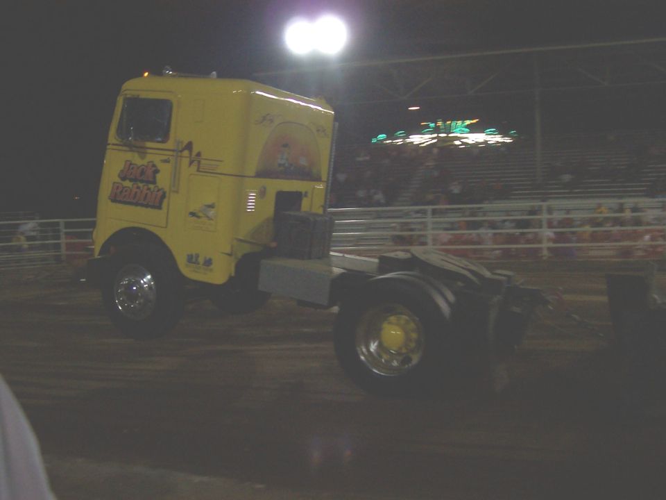 Yellow semi-truck cab with 'Jack Rabbit' text and graphics, parked at an event with stadium seating in the background