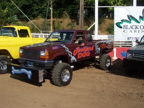 1994 Ford F-150 - A heavily modified pickup truck with custom paint and lifted suspension is parked next to other vehicles.