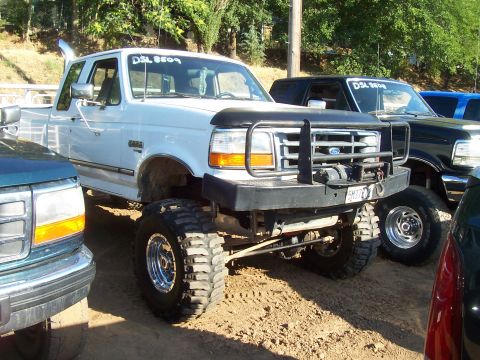 1994 Ford F-150 - A lifted white Ford F-150 pickup truck is parked next to other vehicles.