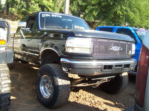 1994 Ford F-150 - This lifted black 1994 Ford F-250 pickup truck is shown from a three-quarter front view, a prominent chrome grille and large off-road tires.