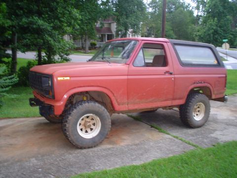1981 Ford Bronco - This red Ford Bronco, likely from the early 1980s, is shown from a three-quarter front angle on a paved surface.