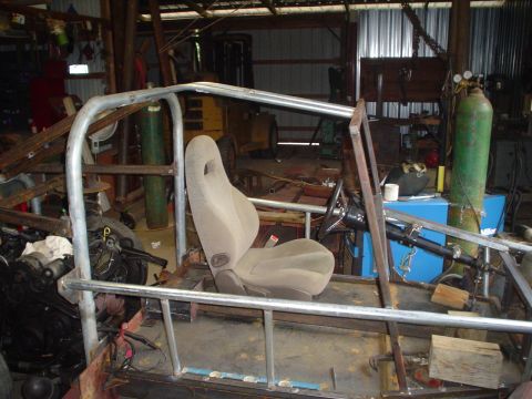1981 Ford Bronco - Custom buggy frame with racing seat and steering wheel in a workshop. Roll cage is visible.