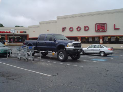 1981 Ford Bronco - Blue Ford F-250 Super Duty truck with large tires parked in a supermarket parking lot.