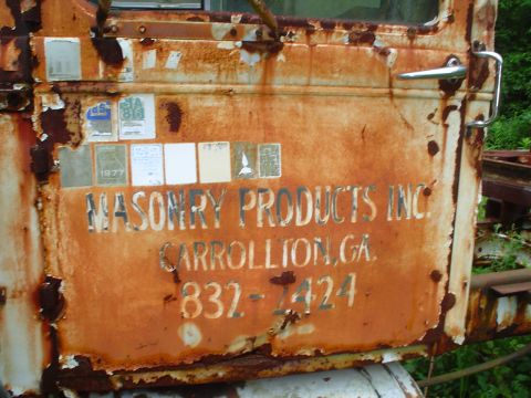 1981 Ford Bronco - This heavily rusted vehicle door displays a "1977" badge and lettering for "MASONRY PRODUCTS INC." in Carrollton, GA.