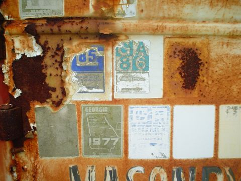 1981 Ford Bronco - Peeling stickers and rust cover a metal surface, showing various years and Georgia vehicle identification.