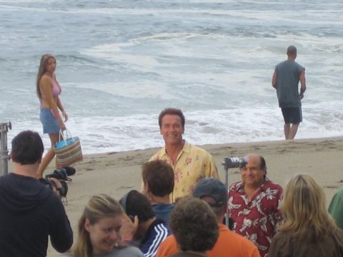 1990 Ford Bronco - crowd and camera crew gather on a beach around a man in a yellow floral shirt by the surf.