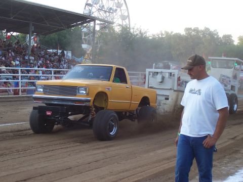 1994 Ford F-150 - A modified yellow pickup truck competes in a pull event, with a spectator observing the action.