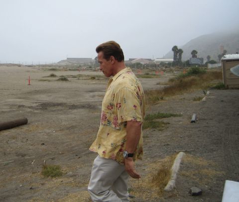 1990 Ford Bronco - man in a yellow floral Hawaiian shirt and tan pants walks across a foggy, barren dirt lot.