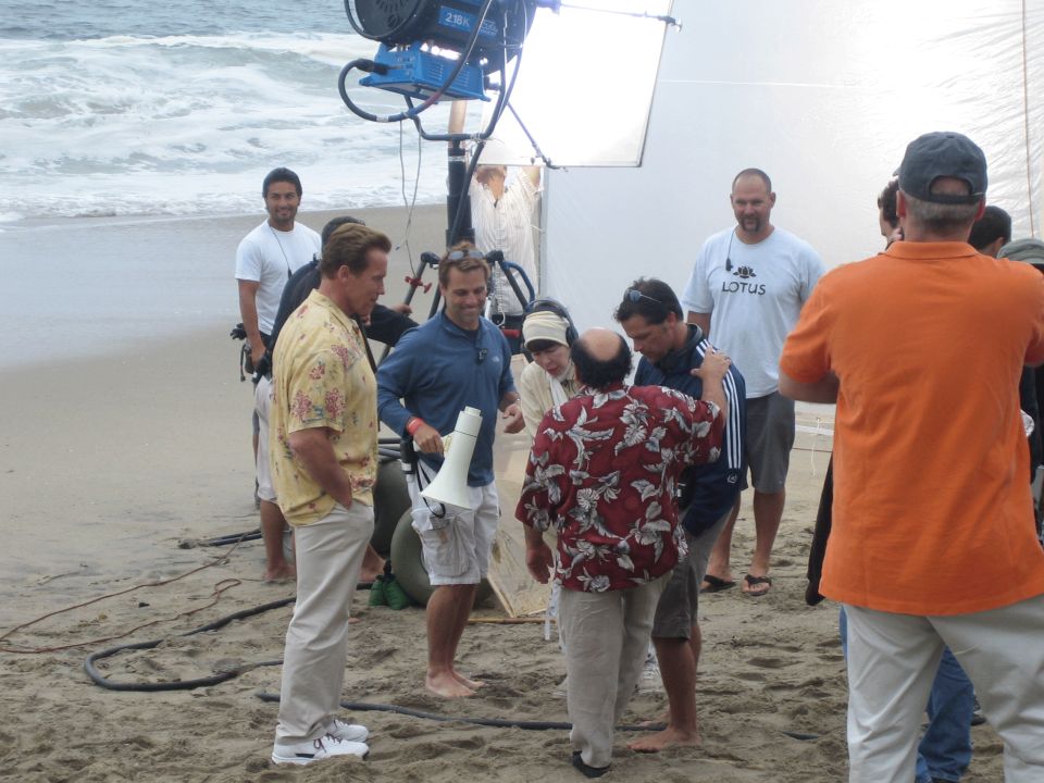 Film crew with a large light and reflector working on a beach with several people
