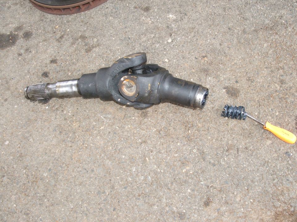 Removed driveshaft slip yoke and U-joint on concrete with yellow-handled cleaning brush