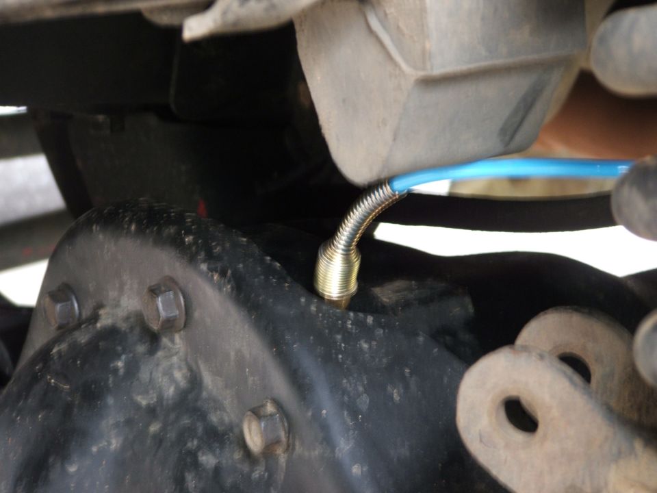 Brass axle vent fitting with blue hose on a black differential housing underside