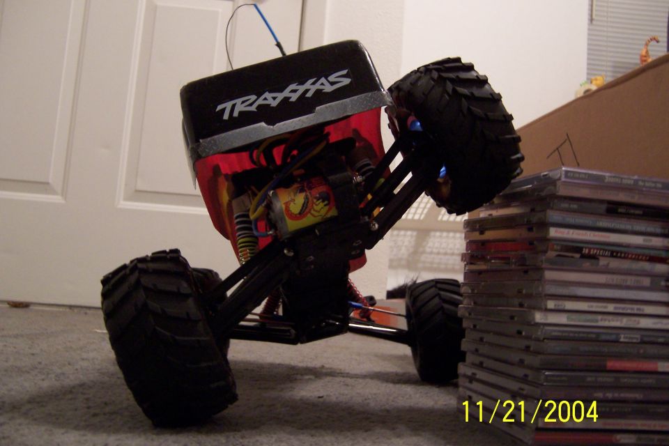 RC monster truck with Traxxas logo, tilted on its side next to a stack of CDs